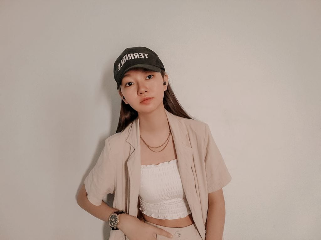 Forside A young woman in a casual outfit and cap poses confidently against a plain background.