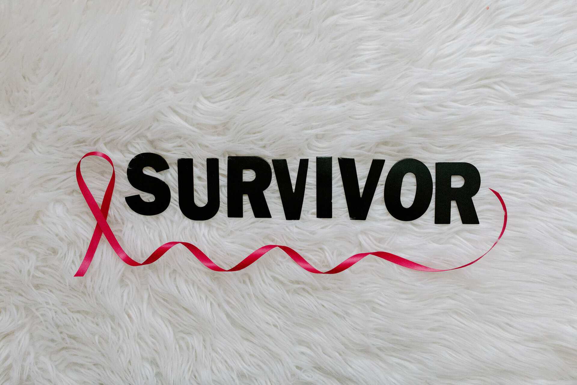 Forside Inspirational image showcasing a pink ribbon next to SURVIVOR text on a soft white background.