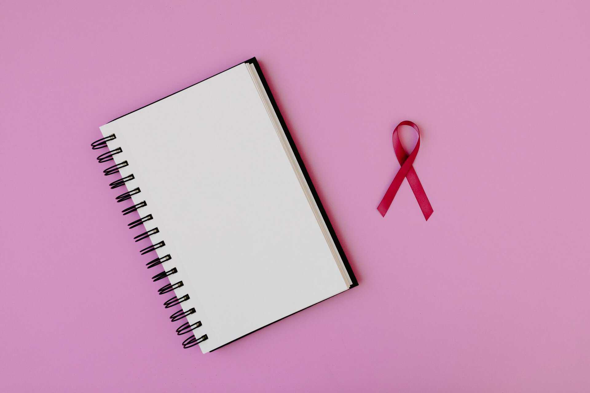 Om forfatteren Open spiral notebook with pink breast cancer awareness ribbon on a pink background, offering copy space.