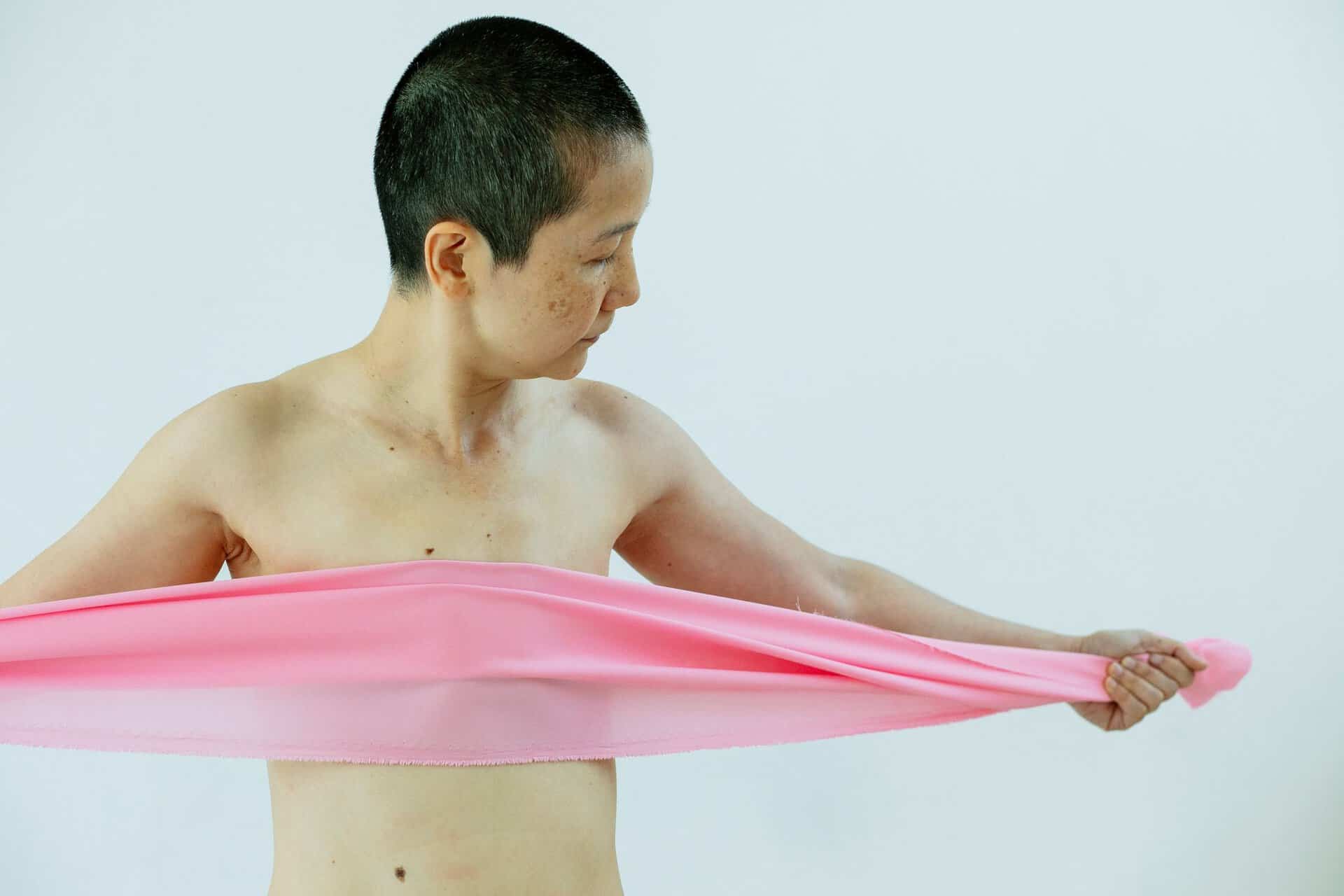 Om forfatteren Topless ethnic woman with short hair spreading pink cloth in hands covering body on white background